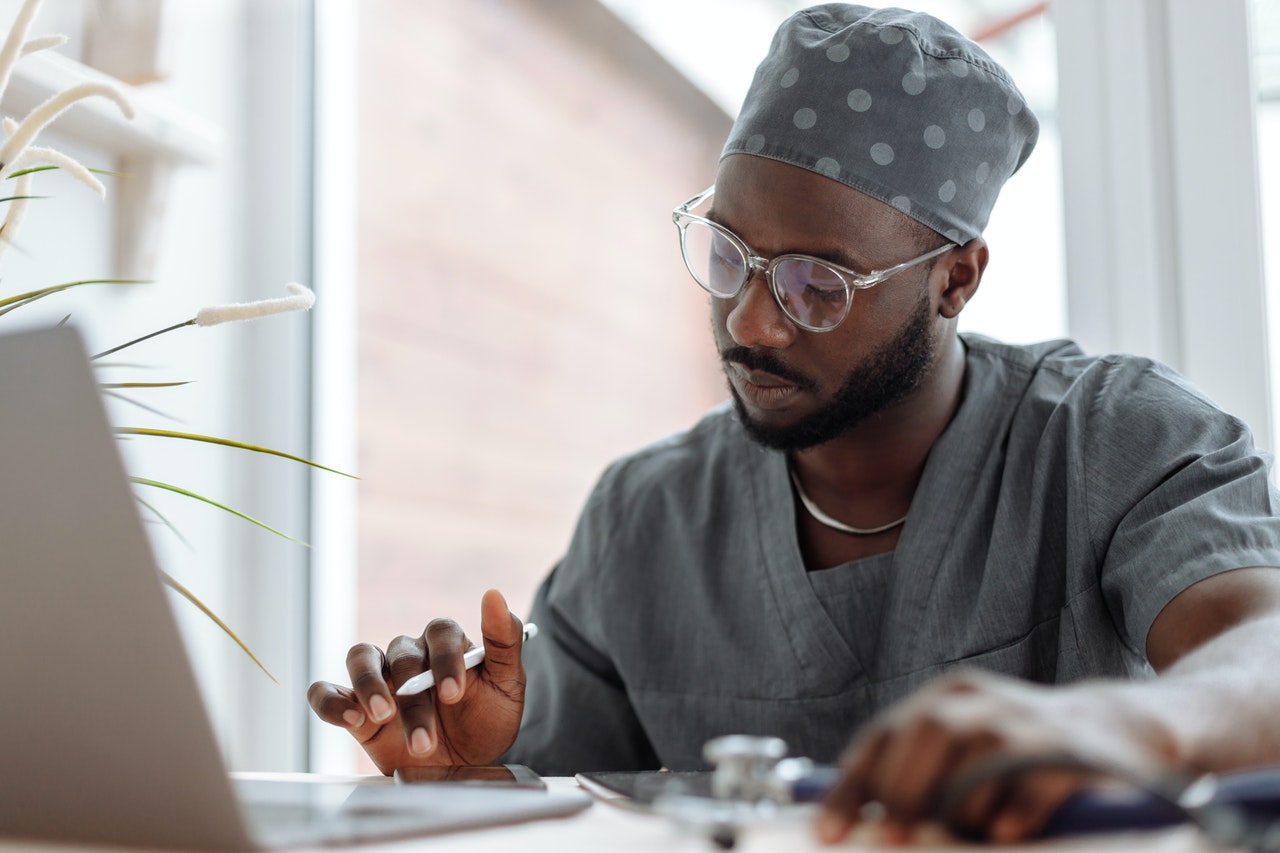 black male doctor in gray scrubs typing on computer