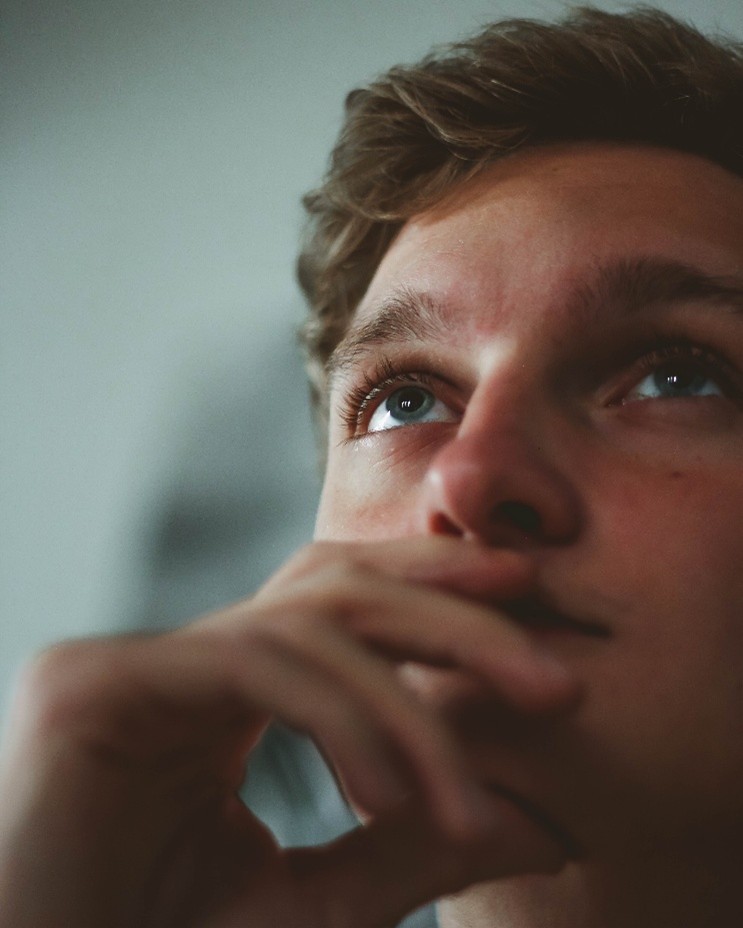 Young man pensively looking up. Or maybe he is just watching a tv we can't see. Who knows. It's a mystery