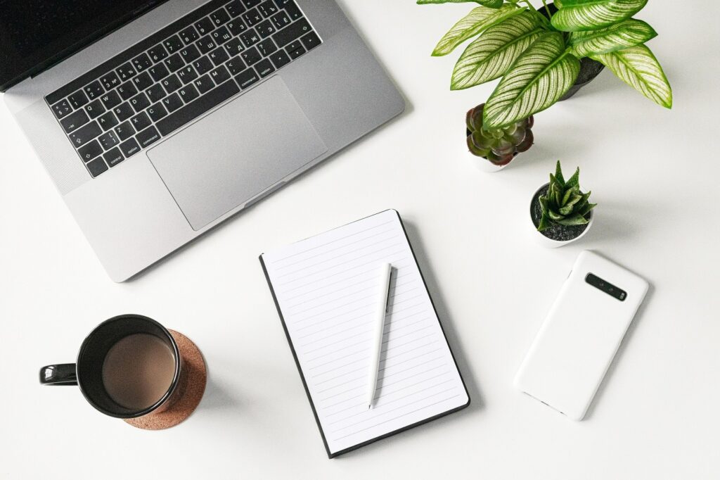 Overhead shot of desk stuff. Laptop, plant, paperclips and a cup of coffee. I bet te coffee is cold. It has to be.