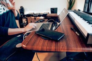 Someone at a desk with a laptop on it. Behind the laptop is a musical keyboard. I don't know why. But it's there.